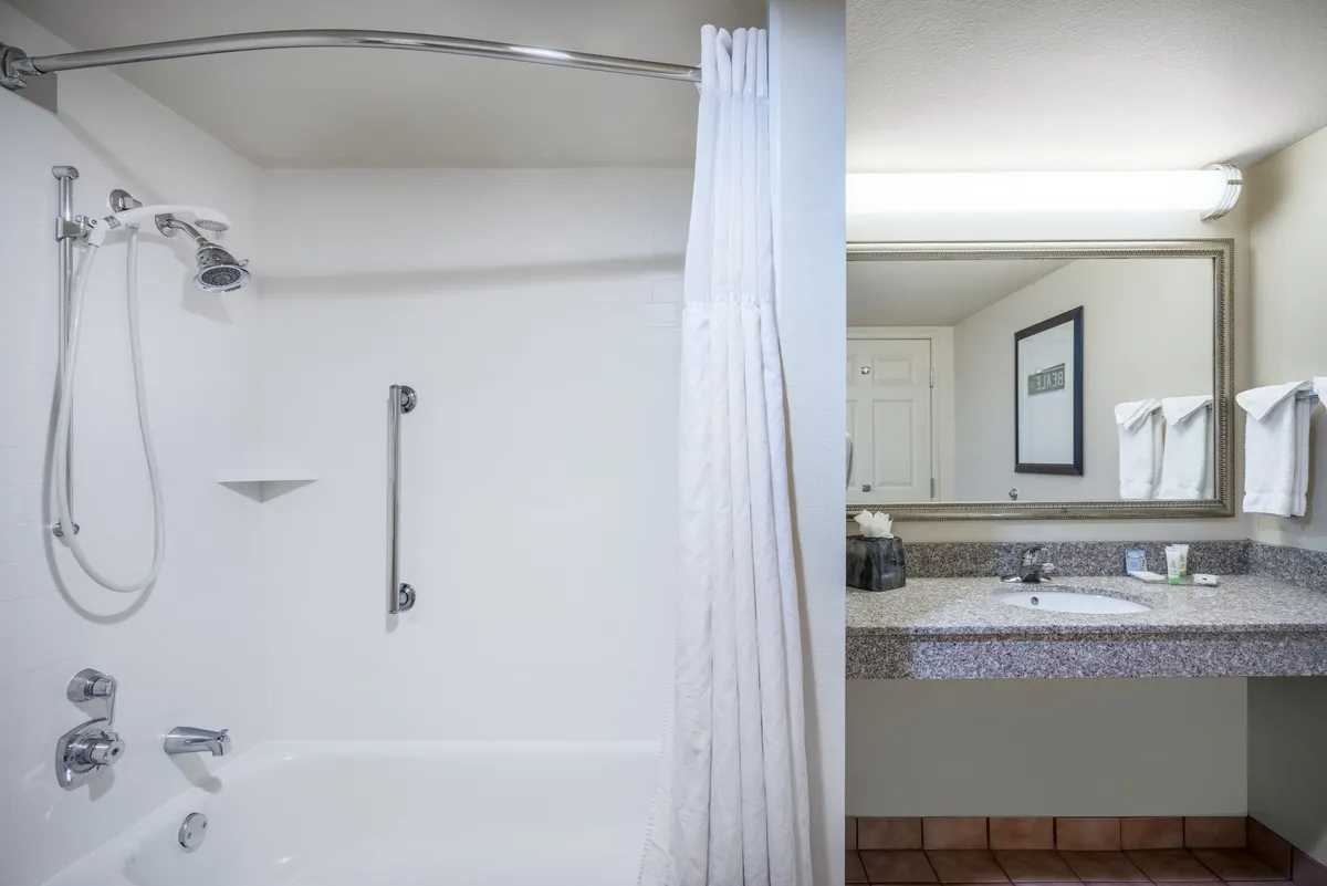 This image features the bathroom interior, centering on the shower area and a vanity with mirror and sink. Soft towels are arranged beside the sink, and the well-lit vanity provides a practical space for personal grooming. The serene atmosphere is highlighted by clean lines and a clutter-free setup, suggesting comfort and convenience.