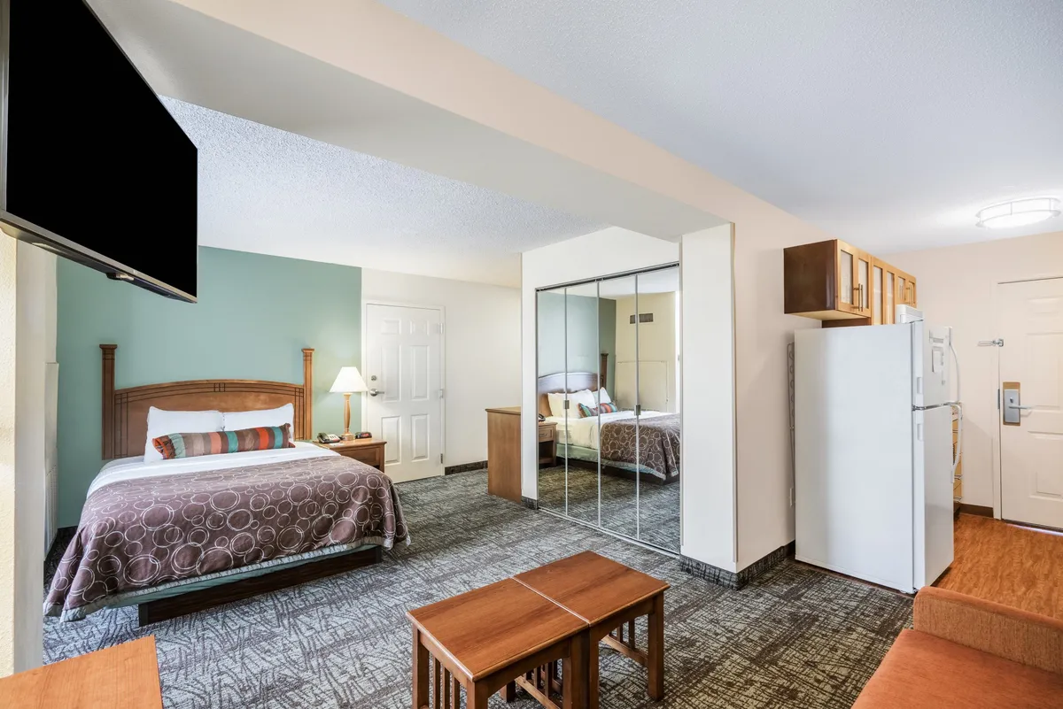 The hero image showcases a cozy, well-lit studio with a plush bed, large mirrored closet, compact refrigerator, inviting seating area, and a TV. The space is thoughtfully arranged to maximize comfort and functionality, perfect for relaxing, enjoying a meal, or unwinding after exploring Memphis.