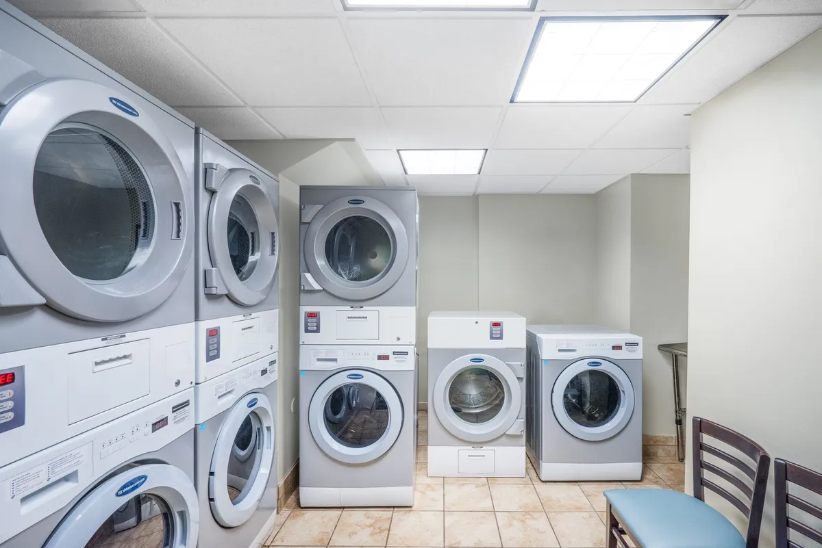 This image captures an interior space featuring several washing machines and dryers, accompanied by a small seating area. The mood is practical, with a focus on cleanliness and everyday routines.