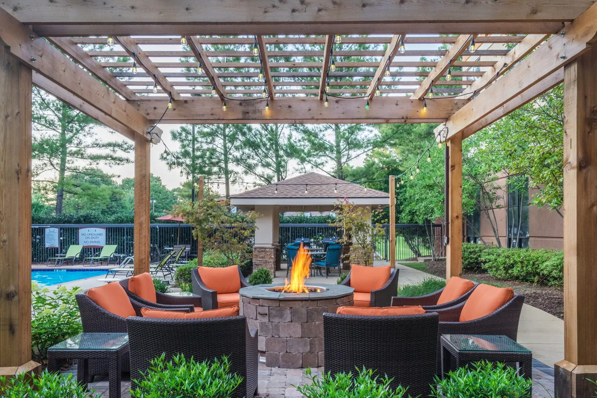 The image captures an inviting outdoor space featuring a cozy fire pit surrounded by comfortable seating under a pergola, adjacent to a sparkling pool area. The atmosphere is lively and communal, with hints of evening social gatherings and opportunities for relaxation by the firelight.