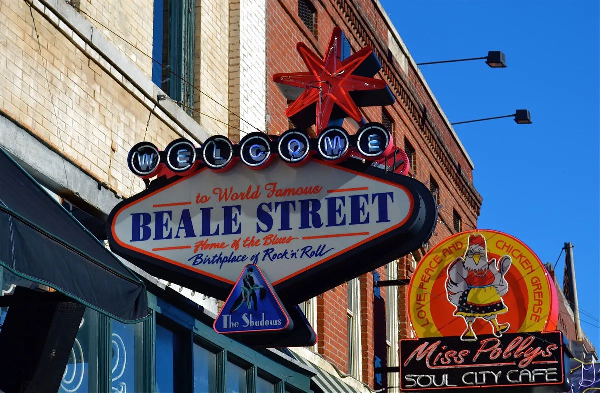 This image captures the vibrant 'Welcome to Beale Street' sign alongside the neon of Miss Polly's Soul City Cafe and The Shadows sign. The lively street scene hints at live music venues, bustling cafes, and a deep sense of Memphis' cultural history, inviting exploration beyond the front door.